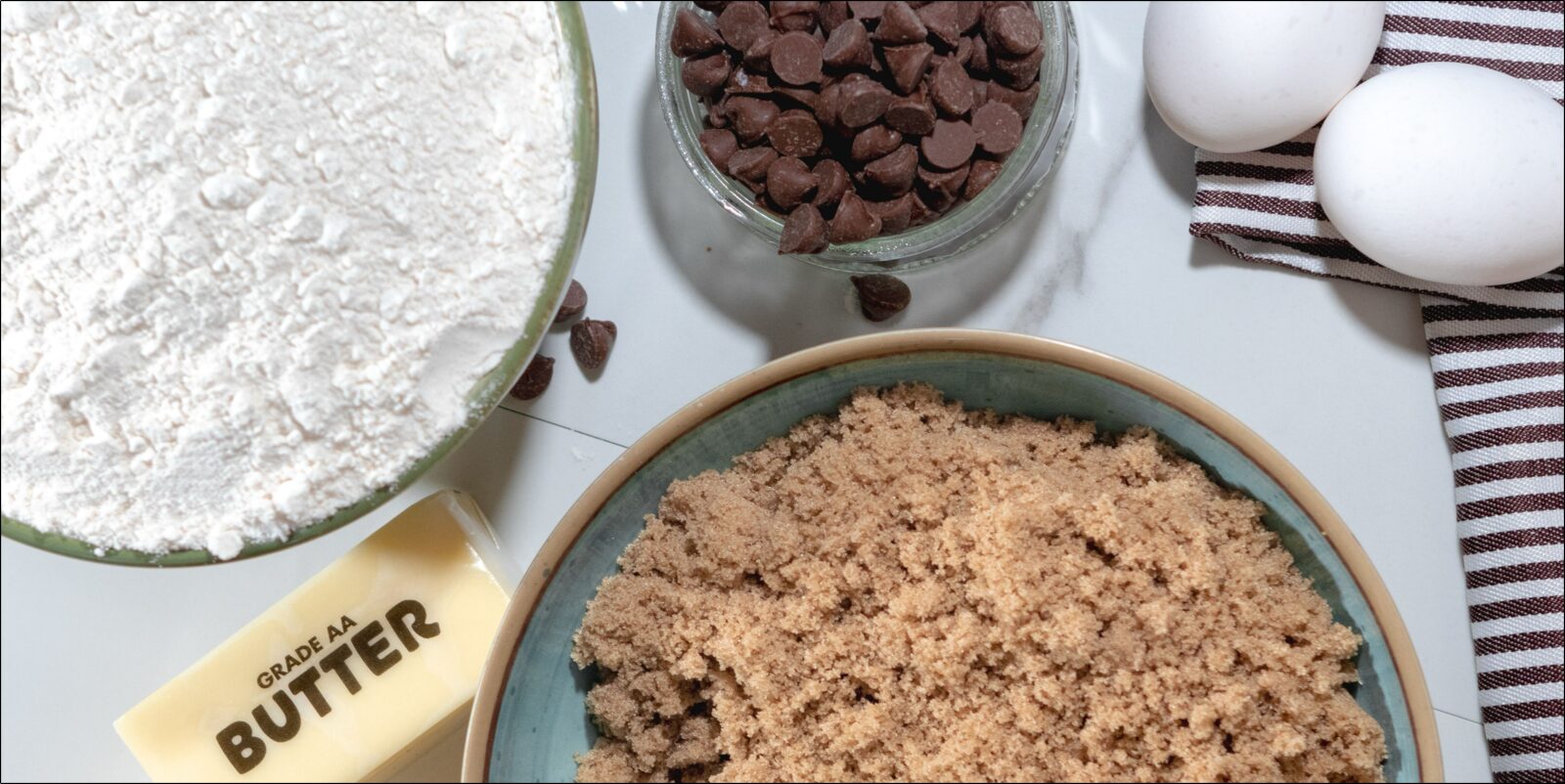 Overhead view of cookie ingredients measured and arranged: flour, butter, brown sugar, chocolate chips, eggs